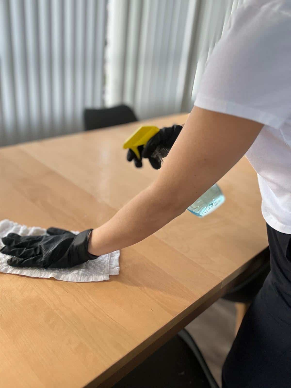 Office desk being cleaned with cloth and spray for a spotless workspace.